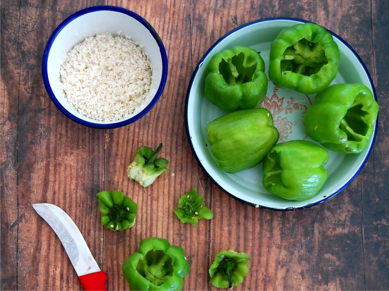 A bowl of uncocked rice with a tray of hollowed out bell peppers. Red handled knife peaking throuh picture