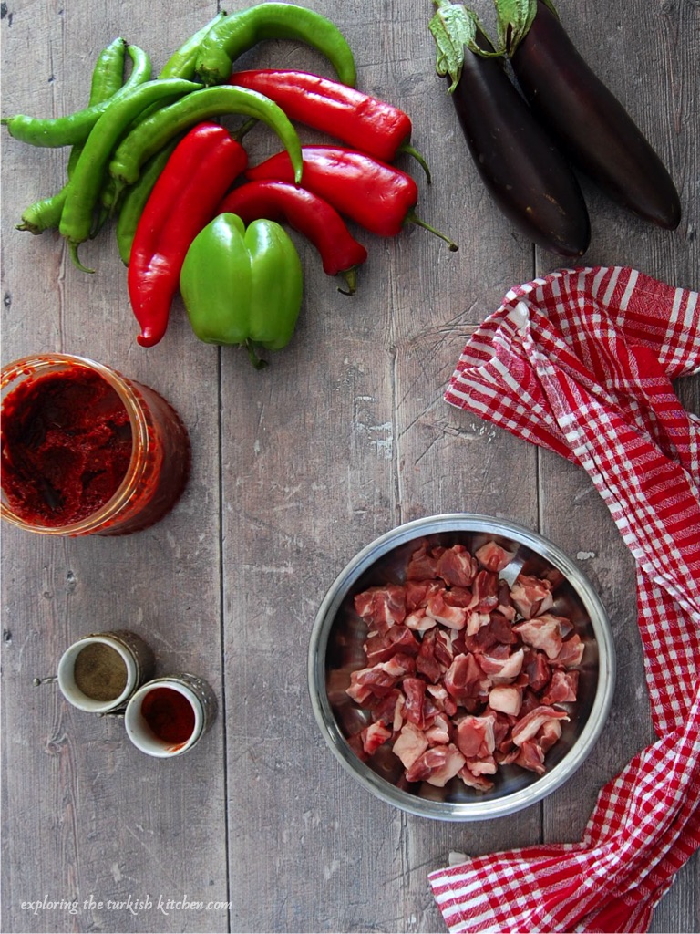Prep table for making Turkish the sutan'd delight casserole. A small bowl of fatty diced meat waits for cooking with fresh red and green peppers, aubergines and seasonings including a tub of red pepper paste. 