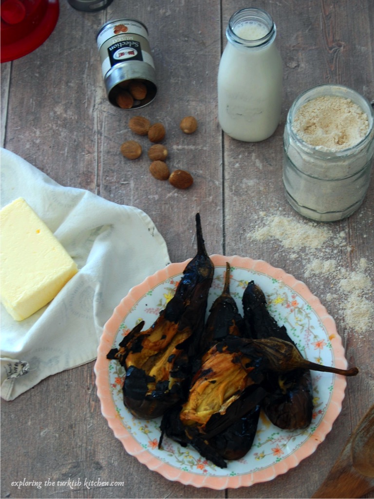Spilt roast aubergines on a vintage Turkish plate surrounded by a jar of flour, a bottle of milk, Ba'dat brand nutmeg and butter. 