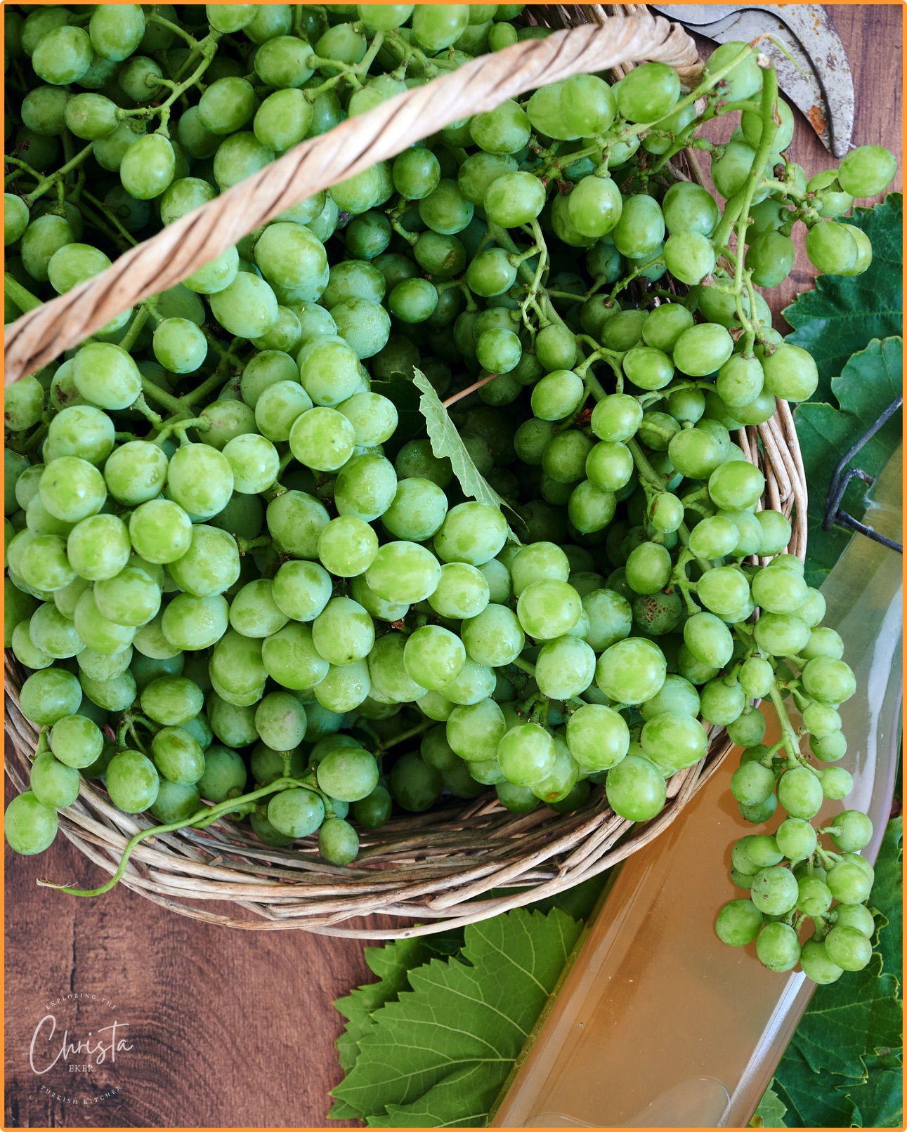Basket of freshly picked Koruk. Unripe grapes and a bottle of verjus laying on vine leaves. 