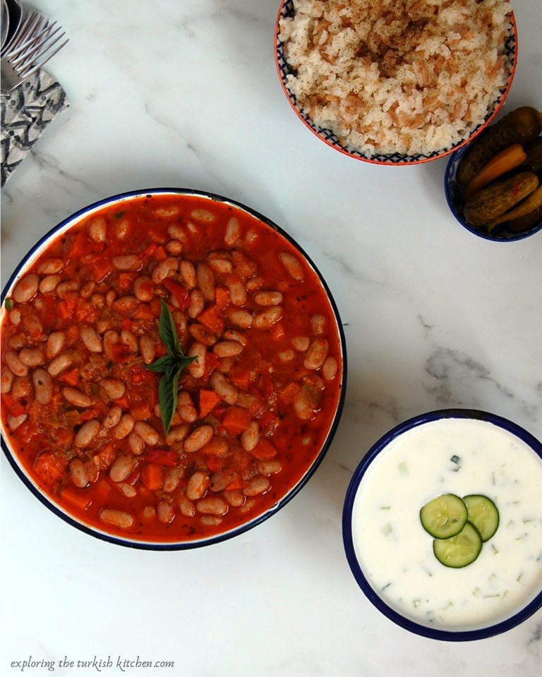 Turkish cranberry beans stew, with a basil leaf served with Turkish rice, cacık, cucumber and yoghurt and Turkish pickles. 