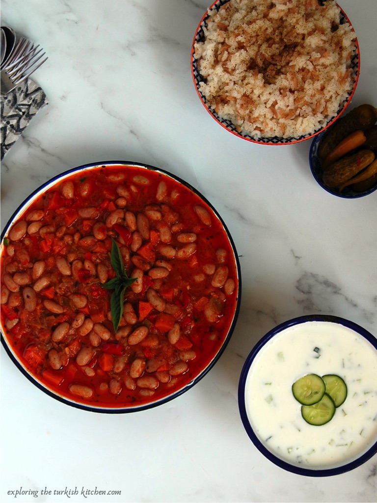 Turkish cranberry bean stew or Borlotti beans with basil garnish served with Turkish rice, cucumber and yoghurt and pickles.