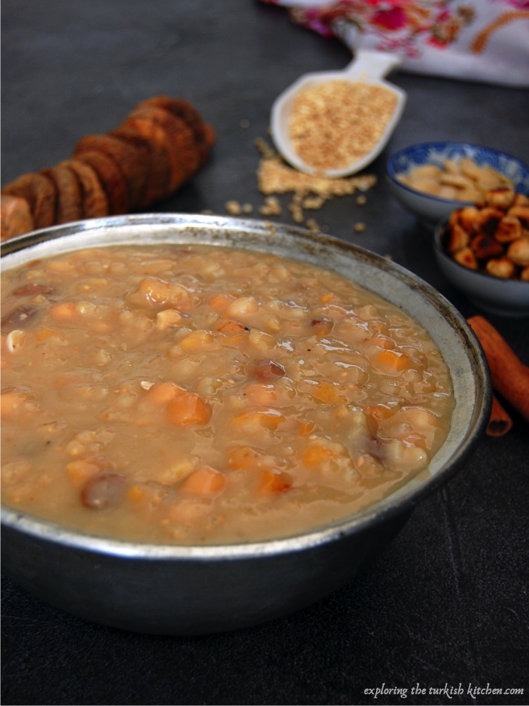 Large bowl of cooked ashure pudding. Ready for dressing and serving. Small bowls of roast and blanched nuts and spices sit aside it.  