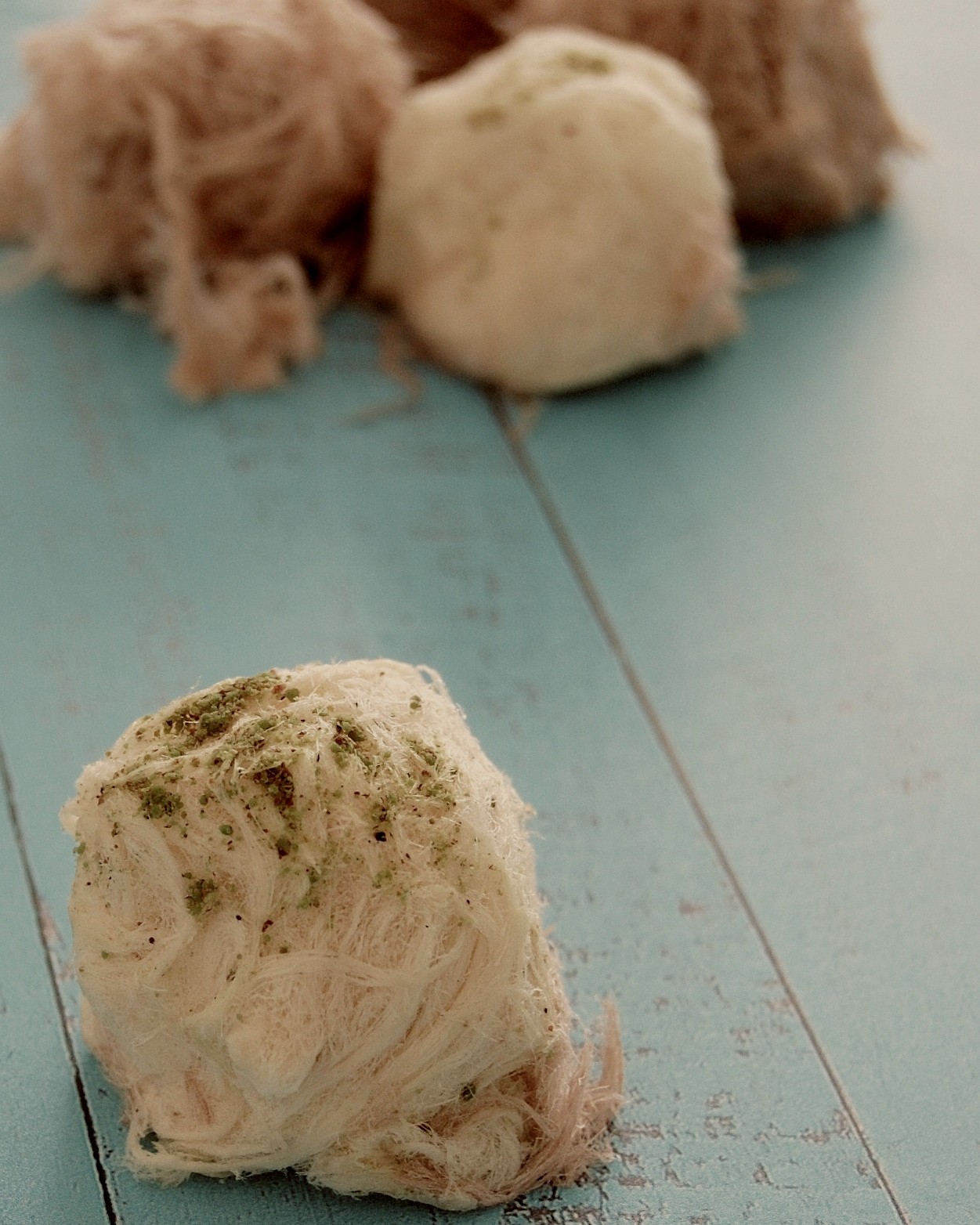 One close up pismaniye hive with ground pistachio on top. Background shows blurred mixed pişmaniyes 