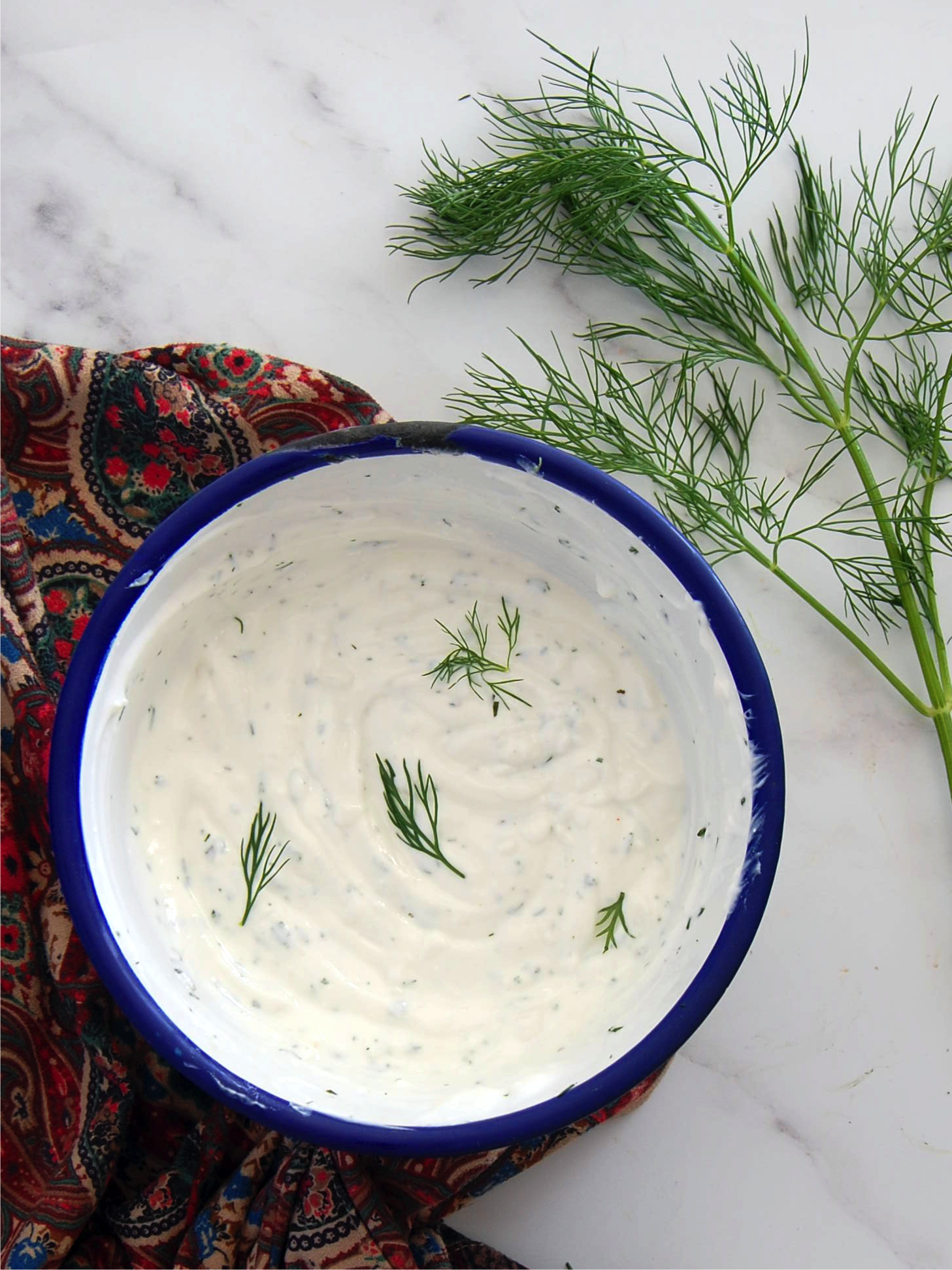 Turkish yoghurt meze piled into a bowl with a scattering of dill fronds. The bowl is surrounded by paisley towel and one dill stem