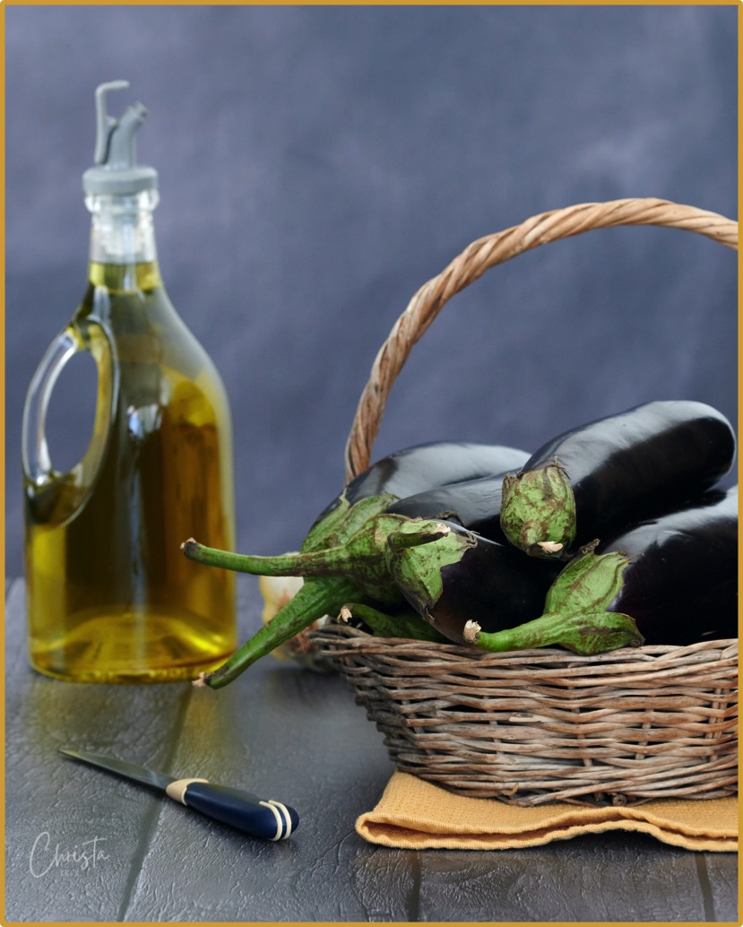 Basket of aubergines, a bottle of Turkish olive oil and vegetable knife on a wooden table. 